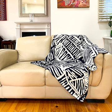 A throw is draped on a couch. The throw features artwork by Jane Margaret Tipumantumirri in black and white.