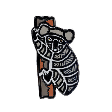 Enamel on metal brooch of a  grey, black and white patterned Australian koala. The koala has black featured on the feet and nose and is positioned on a trunk. 