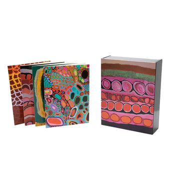 Four greeting cards are pictured on the left overlapping each other. They feature colourful Indigenous artwork by Mornington Island Art. The box is pictured on the right and has artwork in the colours of pink, green and red.