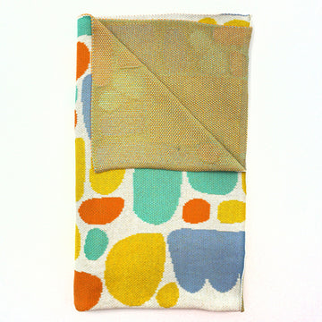 A blanket with artwork by Keturah Nangala Zimran featuring blue, yellow and green shapes. A corner is folded over to show the yellow back.