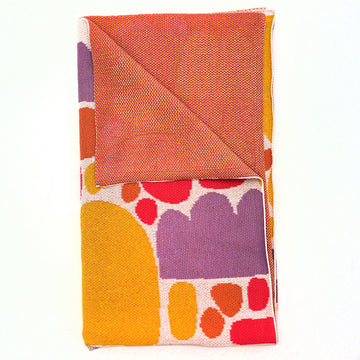 A blanket featuring artwork by Keturah Nangala Zimran in yellow and purple shapes. The corner is folded over to show the orange back.