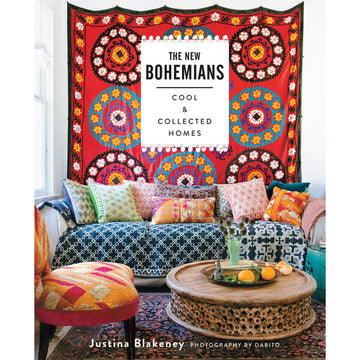 'The New Bohemians' book cover featuring a photo of a couch covered with different coloured cushions and a large wall hanging behind. There is a single chair and a round wooden coffee table in front of the couch on a rug.