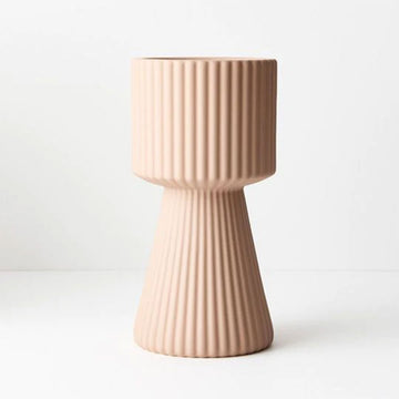 A tall vase with a triangular bottom half and round top half in nude with embossed vertical lines.