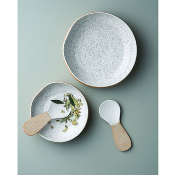 A round bowl with an imperfect shape made from stoneware and printed with a speckled pattern. The inside of the bowl is white and the outside is light brown.