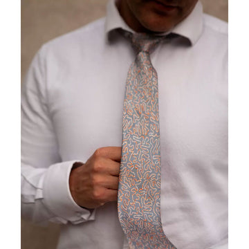 A rolled up tie printed with artwork by Kumanjayi Jurra in orange and white dots on a grey background.