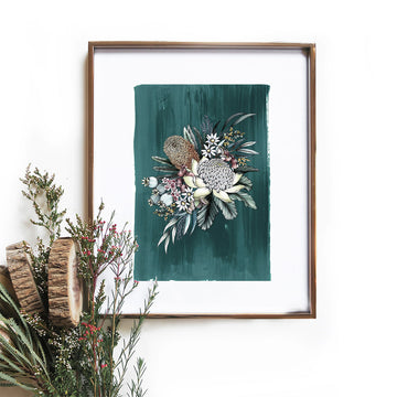 A framed print of a bunch of native flowers in the centre of a teal background surrounded by a thick white border. There are a few stems in front of the frame.