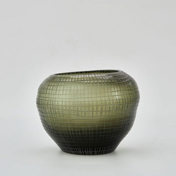 A round vase in moss green glass with a grid pattern on it. The top is uneven with the right side higher than the left.