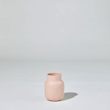 A small ceramic bottle in pink against a grey background.