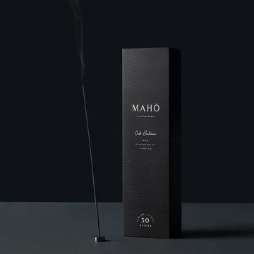 A black tall rectangle box with the text 'Maho A little Magic' written in white. There is an incense stick burning next to the box.