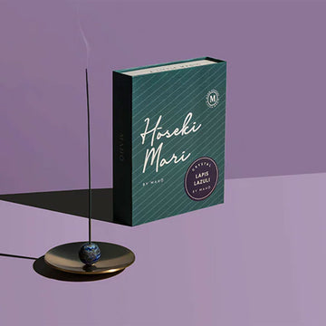 An incense stick is burning on a brass dish and there is a green box behind with the text 'Hoseki Mari' in white.