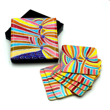 A set of six coasters are lying on top of each other next to the open box. The coasters and box lid feature artwork by Liddy Napanangka Walker in yellow, pink and brown.