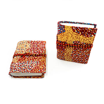 Two small notebooks pictured with red rope around them and printed with artwork by&nbsp;Lynette Nangala Brown&nbsp;on the covers. One notebook is lying flat and the other is standing up.