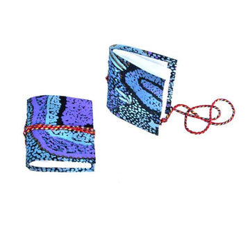 Two small notebooks pictured with red rope around them and printed with artwork by Pauline Nampijinpa Singleton on the covers. One notebook is lying flat and the other is standing up.