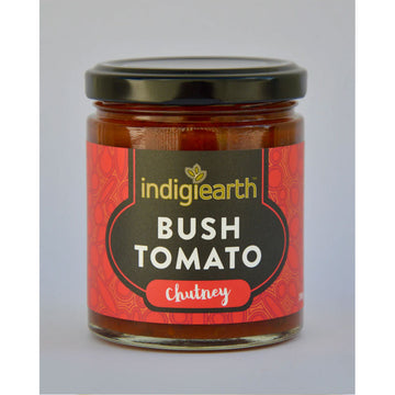 A clear jar with a black lid and wide product label. The label says 'Indigiearth Bush Tomato Chutney' on a red and black background.