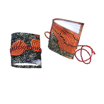 Two small notebooks pictured with red rope around them and printed with artwork by&nbsp;Damien and Yilpi Marks on the covers. One notebook is lying flat and the other is standing up.