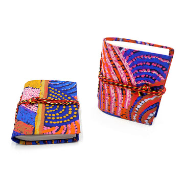 Two small notebooks pictured with red rope around them and printed with artwork by Nora Nyutjanka Davidson on the covers. One notebook is lying flat and the other is standing up.