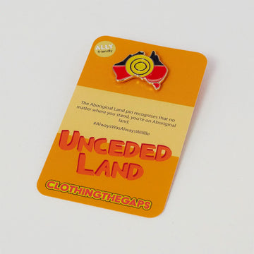 A pin in the shape of Australia in the Aboriginal flag on an orange product card. The card says 'Unceded Land Clothing the Gaps'.