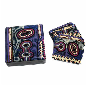 A set of coasters are laying overlapping each other on the right with a matching square box on the left. The coasters and box are both printed with artwork by Murdie Nampijinpa Morris in purple and red.