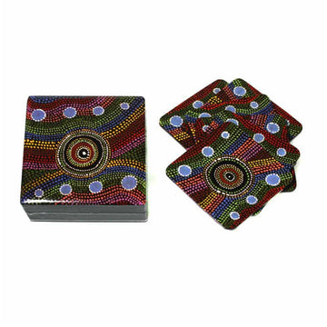 A set of coasters are laying overlapping each other next to a matching square box. The box and coasters are printed with artwork by Yaritji Heffernan with multicoloured dots in the background and larger circle in the middle made from dots.