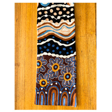 A birds eye view of a table runner made from wool chain stitch on a wooden table. The table runner features artwork by Bianca Gardiner-Dodd with blue and orange flowers, arches and dots.