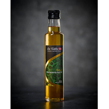 A clear glass bottle filled with oil and a black lid with a product label on the front. The label says 'Natural Macadamia Nut Oil'.
