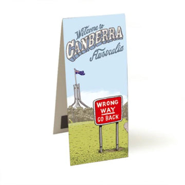 A magnetic bookmark standing open and printed with artwork by Trevor Dickinson of a sign 'Wrong Way Go Back' with Parliament House in the background. The heading 'Welcome to Canberra Australia' is at the top.