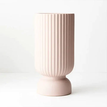 A tall vase with a rounded base in light pink. There are vertical embossed lines on the vase.
