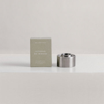 A stainless steel oil burner next to a green packaging box.