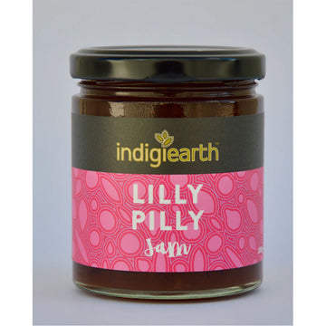 A clear jar with a black lid and wide product label. The label says 'Indigiearth Lilly Pilly Jam' on a black and pink background.