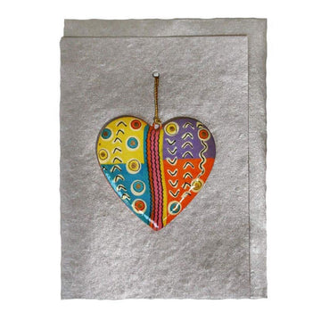 A silver greeting card with a matching envelope behind. There is a heart shaped ornament on the front of the card printed with artwork by Judy Watson.