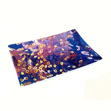 A rectangle shaped ceramic plate printed with artwork by Stephen Jupurrula Nelson in blue, yellow and red.