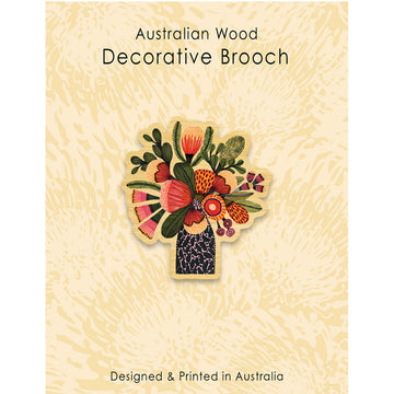 A wooden brooch in the shape of flowers in a vase on a light brown patterned background with the heading 'Australian Wood Decorative Brooch'.