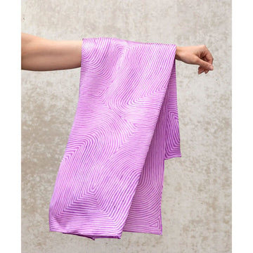 A pink silk scarf is laying flat and printed with a swirl pattern in artwork by George Tjungurrayi.