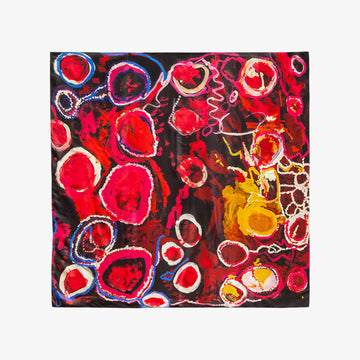 A square silk scarf printed with artwork by Jimmy Donegan in red, yellow and blue on a black background is laying flat.