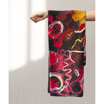 A square silk scarf printed with artwork by Jimmy Donegan in red, yellow and blue on a black background is laying flat.