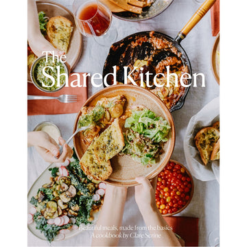 'The Shared Kitchen' book cover featuring a photo of a top down view of a table filled with plates of food and hands holding a dish above the table while another person takes food off the plate.