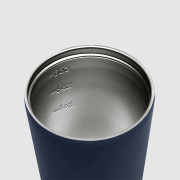 A reusable coffee cup in a denim blue with a black lid. The text 'made by Fressko' is written on the bottom of the cup.