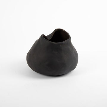 A handcrafted vase in black in an irregular round shape.