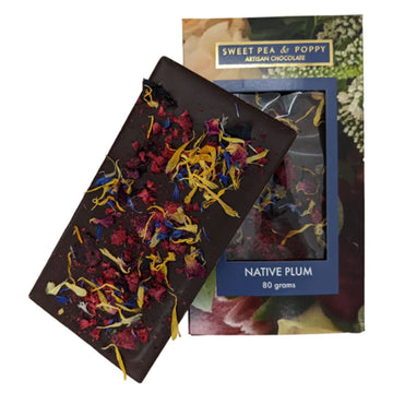 A block of chocolate is leaning against its packaging box. The chocolate has fruits and flowers attached to it and the box is printed with flowers with a window in the middle showing the chocolate inside.