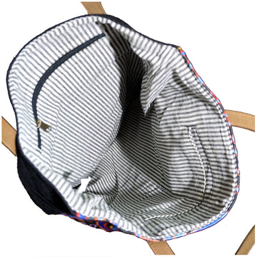 A green, yellow and blue tote bag featuring artwork by Cedric Varcoe with brown handles.