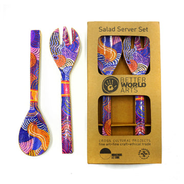 A pair of wooden salad servers printed with artwork by Nora Nyutjanka Davidson on the front is pictured twice. One set is on the left and the set on the right is inside a cardboard box.