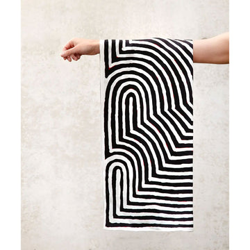 A black and white silk scarf laid out featuring artwork by Aubrey Tjangala.