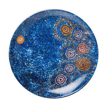 A round ceramic plate printed with artwork by Alma Granites. The artwork is dark blue with yellow and white circles.
