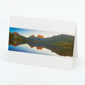 A white landscape greeting card with a panoramic photograph of Dove lake and Cradle mountain with the mountains reflected in the lake.