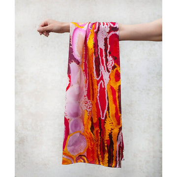 A silk scarf is laid out featuring artwork by Jakayu Biljabu in pinks, reds and yellow.