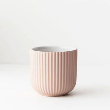 A small ceramic pot in light pink with lines on the outside.