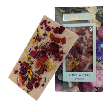 A block of chocolate is leaning against its packaging box. The chocolate has red berries and flowers attached to it and the box is printed with flowers with a window in the middle showing the chocolate inside.