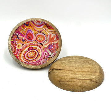 A wooden trinket dish printed with artwork by Cedric Varcoe on the inside is standing up. Another dish is laying flat down.