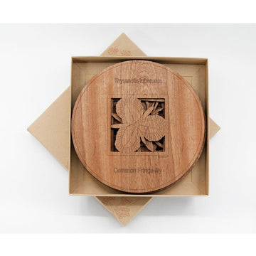 An open box with a set of wooden round table mats. The mats have a cut out of a flower in the middle.