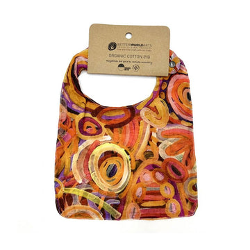 A cotton baby bib printed with artwork by Cedric Varcoe and a brown product tag at the top.